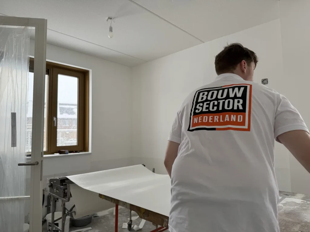 Behanger van Bouwsector Nederland rolt een baan vlies uit over de plaktafel in een lege nieuwbouwkamer
