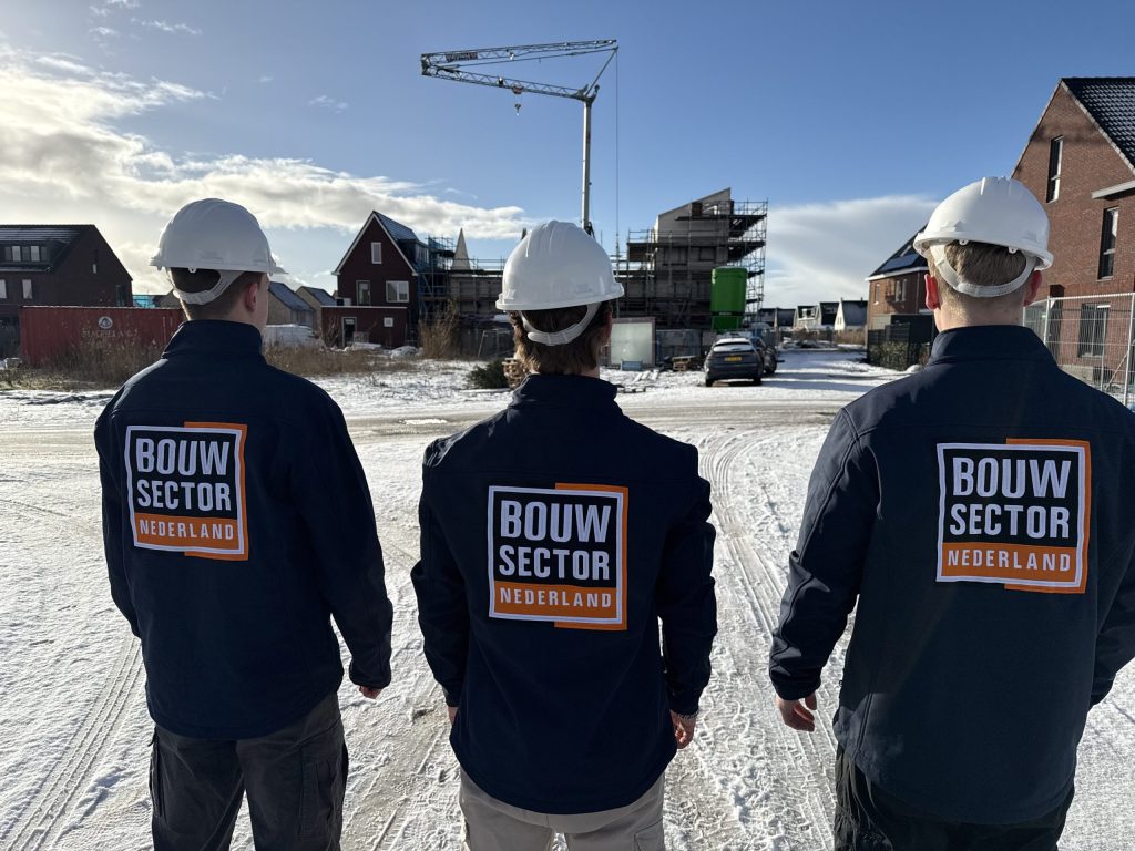 Drie vakmensen van Bouwsector Nederland met witte helm bij een nieuwbouwstraat met een bouwkraan